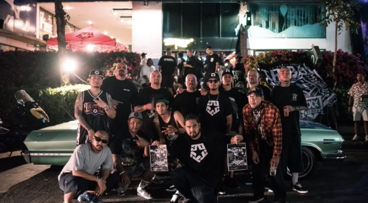 Large Asian Barrio crew portrait beside a lowrider at night